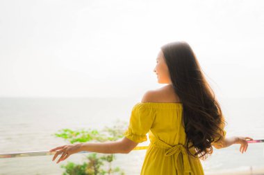 Portre güzel genç Asyalı kadın mutlu gülümseme ve boş zaman seyahat ve tatil için deniz plaj ve okyanus manzaralı açık balkon dinlenin