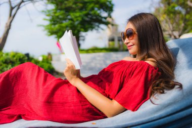 Otel ve tatil tatil konsepti için Resort yüzme havuzunda portre güzel genç Asyalı kadın okuma kitabı