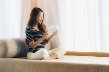 Portre güzel genç Asya kadın okuma kitap içinde üzerinde kanepe içinde 