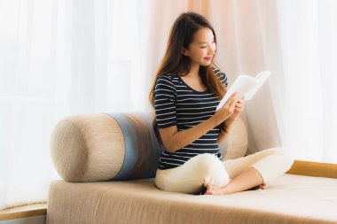 Portre güzel genç Asya kadın okuma kitap içinde üzerinde kanepe içinde 