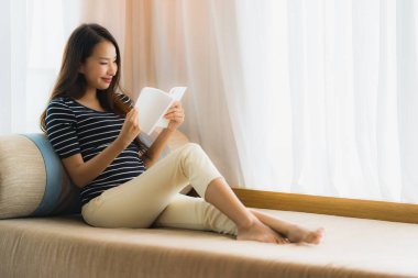 Portre güzel genç Asya kadın okuma kitap içinde üzerinde kanepe içinde 