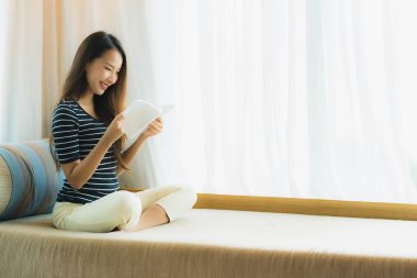 Portre güzel genç Asya kadın okuma kitap içinde üzerinde kanepe içinde 