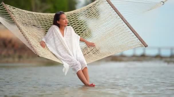 夏休み中に海岸のハンモックに横たわっている美しいアジアの女性の映像 — ストック動画