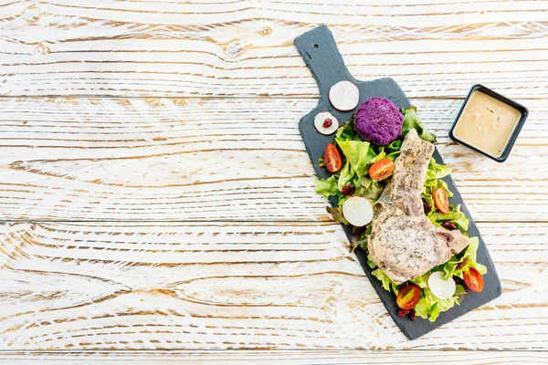 Стейк со свининой на гриле на черной тарелке с овощами — стоковое фото