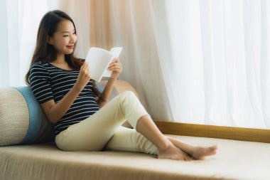 Portre güzel genç Asya kadın okuma kitap içinde üzerinde kanepe içinde 