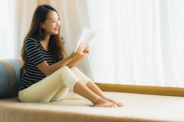 Portre güzel genç Asya kadın okuma kitap içinde üzerinde kanepe içinde 