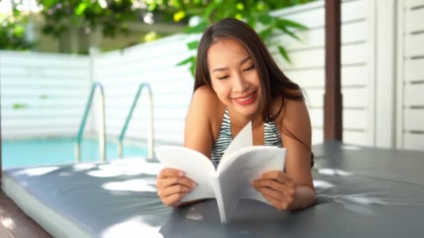美丽的亚洲女人在酒店游泳池放松和阅读书籍的镜头 — 图库视频影像