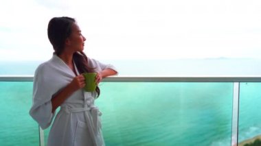 Güzel bir Asyalı kadının balkonda kahve içerken çekilmiş görüntüleri.