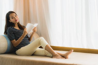 Portre güzel genç Asya kadın okuma kitap içinde üzerinde kanepe içinde 