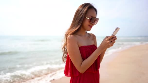 夏休み中に海岸でスマートフォンを使用して美しいアジアの女性の映像 — ストック動画