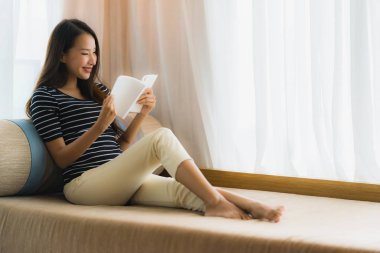 Portre güzel genç Asya kadın okuma kitap içinde üzerinde kanepe içinde 