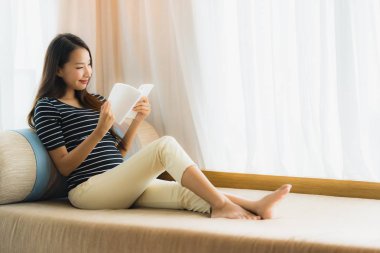 Portre güzel genç Asya kadın okuma kitap içinde üzerinde kanepe içinde 