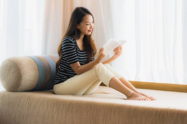 Portre güzel genç Asya kadın okuma kitap içinde üzerinde kanepe içinde 