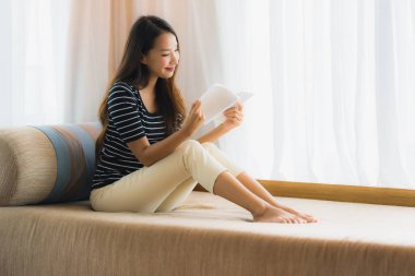 Portre güzel genç Asya kadın okuma kitap içinde üzerinde kanepe içinde 