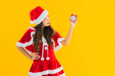 Güzel bir Asyalı kadın portresi Noel kıyafetleri ve şapka gösterisi saati giyer ya da sarı izole arka planda alarm çalar.