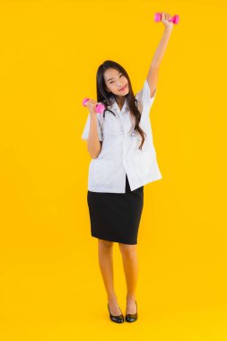 Güzel Asyalı genç doktor kadın portresi. Sarı izole arka planda dambılla egzersiz yapıyor.