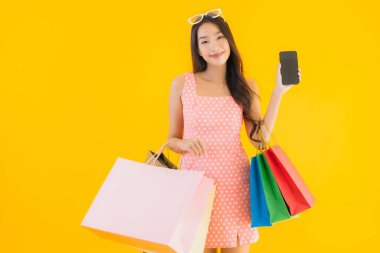 Renkli alışveriş çantalı güzel Asyalı kadın akıllı cep telefonu ve sarı izole edilmiş arka planda kredi kartı.
