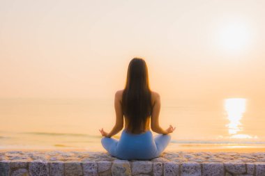 Genç Asyalı kadının portresi sağlık için gün doğumunda deniz kıyısı okyanusunda meditasyon yapıyor.