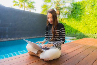 Genç Asyalı bir kadının portresi oteldeki yüzme havuzunda dizüstü bilgisayar kullanıyor.