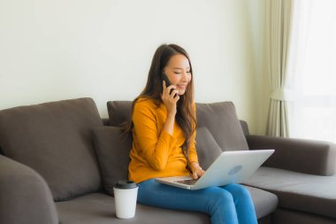 Laptop bilgisayar kullanan Asyalı genç bir kadının portresi. Akıllı cep telefonu ve kahve fincanı olan bir defter.