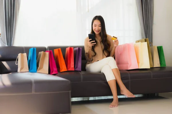 신용카드와 스마트폰으로 온라인 쇼핑을 아름다운 아시아 여성의 거실에 쇼핑백을 봅니다 — 스톡 사진