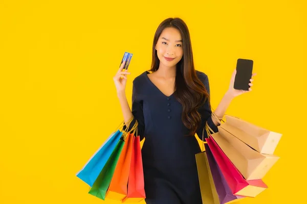 具有购物袋信用卡和智能手机黄色背景的漂亮年轻亚洲女人的肖像 — 图库照片