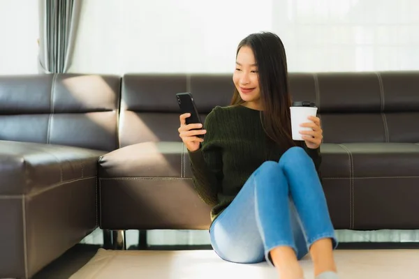 亚洲年轻貌美的女人在客厅里用装有咖啡杯和沙发的智能手机 — 图库照片
