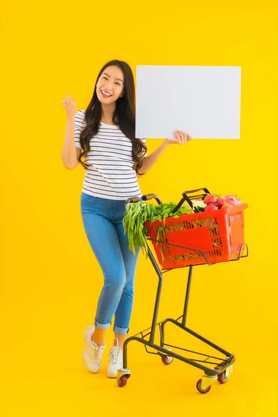 形象美丽的年轻亚洲女人 提着购物篮车 在黄色孤立的背景上展示白色空板 — 图库照片