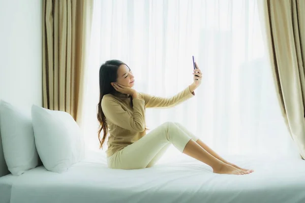 Young asian woman using mobile smart phone on bed in bedroom interior