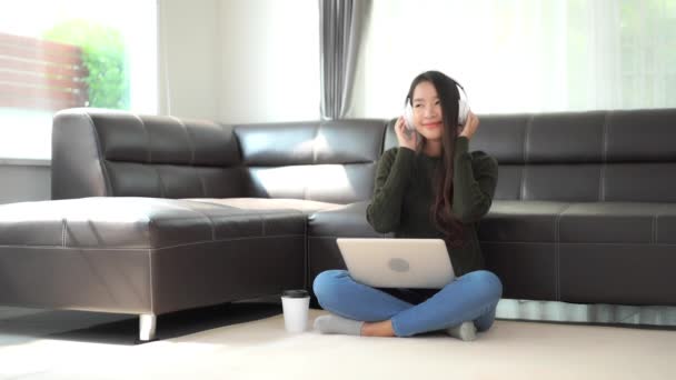 ノートパソコンやヘッドフォンで音楽を聴いている美しいアジア系女性の映像です — ストック動画