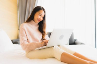 Yatak odasının iç kısmında dizüstü bilgisayarı ve cep telefonu olan güzel Asyalı kadın portresi.