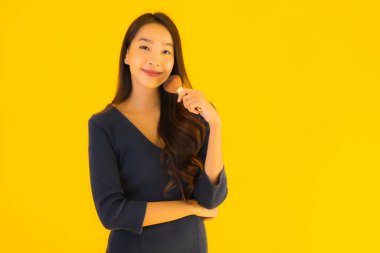 Sarı izole arkaplanda makyaj fırçası olan güzel bir Asyalı kadın portresi.