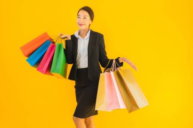 Sarı izole edilmiş arka planda alışveriş merkezinden alışveriş çantasıyla güzel bir genç Asyalı kadın portresi.