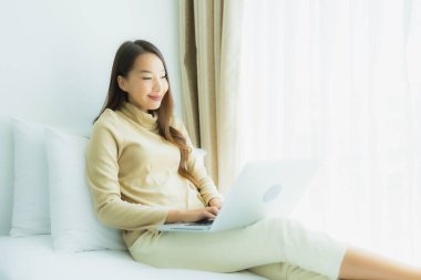 Genç Asyalı kadın yatak odasında dizüstü bilgisayar kullanıyor.