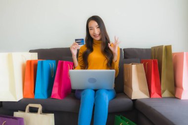 Genç Asyalı kadının oturma odasında online alışveriş yapmak için akıllı cep telefonu ve kredi kartı olan dizüstü bilgisayarı kullandığı portre.