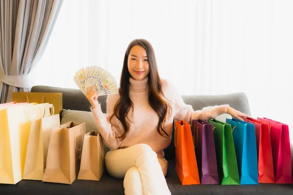 リビングルーム内のショッピングバッグの周りのソファの上でオンラインショッピングのためのラップトップやスマート携帯電話を使用して美しい若いアジアの女性の肖像画 — ストック写真