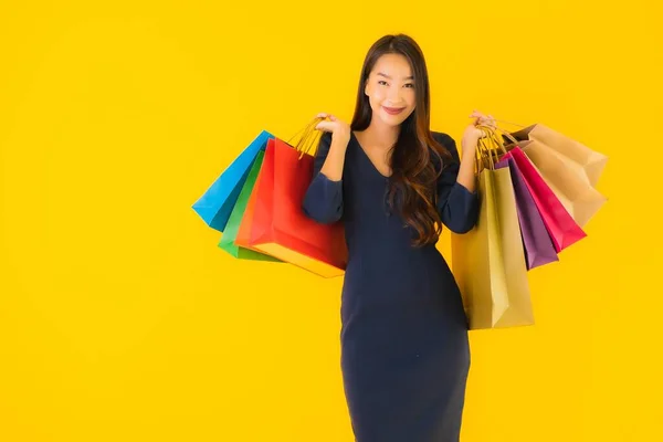 黄色の隔離された背景にカラフルなショッピングバッグを持つ肖像画の美しい若いアジアの女性 — ストック写真