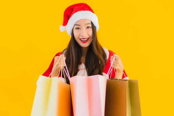 肖像画美しい若いアジアの女性は 黄色の隔離された背景に買い物袋の多くとクリスマス服の帽子を着用 — ストック写真