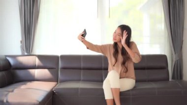 Güzel Asyalı kadının evde akıllı telefonuyla selfie çektiği görüntüler.