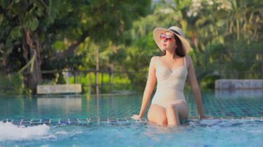Güzel Asyalı bir kadının, tatil için otel tatil beldesinde yüzme havuzunda dinlendiği görüntüler.