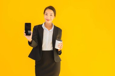 Portre güzel genç Asyalı kadın akıllı cep telefonu ve kahve fincanı ile izole edilmiş sarı arka planda