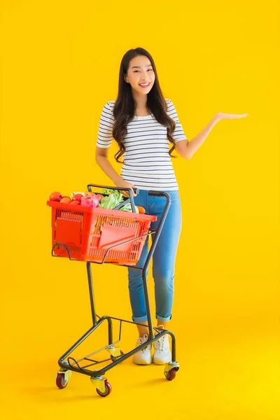 노란색외진 배경에 슈퍼마켓 카트에서 식료품을 아름다운 아시아 여자의 — 스톡 사진