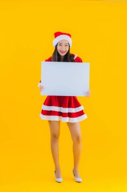 Güzel genç Asyalı kadın portresi Noel kıyafetleri ve sarı izole edilmiş arka planda boş beyaz pano işareti olan şapka gülüşü.