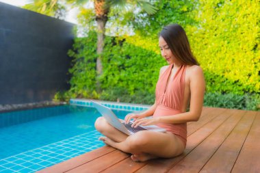 Genç Asyalı bir kadının portresi oteldeki yüzme havuzunda dizüstü bilgisayar kullanıyor.