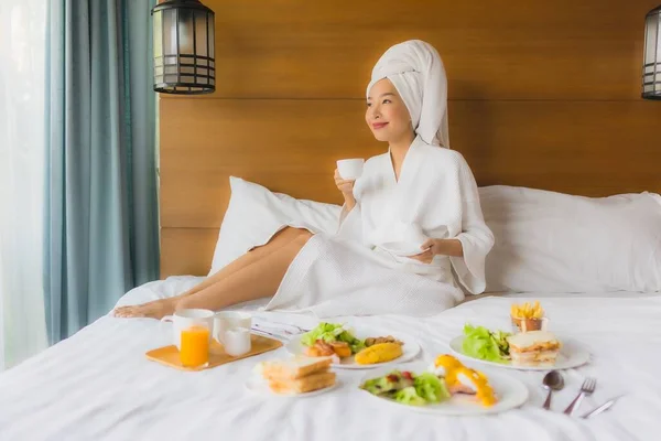 照片中年轻的亚洲女人躺在床上 在卧室里吃早餐 — 图库照片