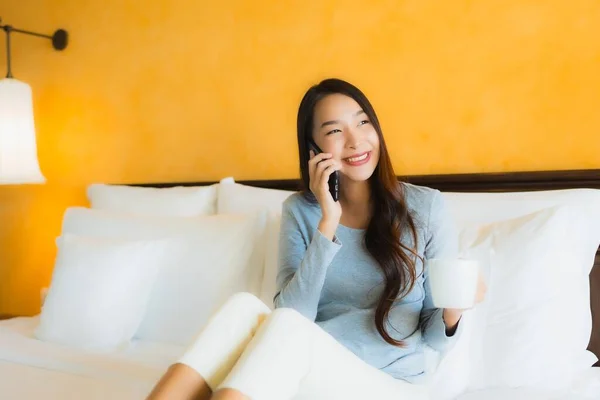 Portrait beautiful young asian woman using mobile cell phone on bed with coffee cup in bedroom interior