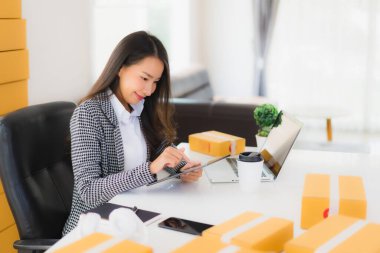 Güzel Asyalı iş kadını portresi evden bilgisayarlı cep telefonuyla karton kutuyla çevrimiçi alışveriş için hazır bekliyor.