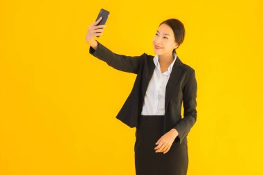 Portre güzel genç Asyalı kadın akıllı cep telefonu ve kahve fincanı ile izole edilmiş sarı arka planda