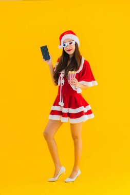 Güzel bir Asyalı kadın portresi patlamış mısır ve 3D gözlüklü noel şapkası takıyor sarı izole edilmiş arka planda film izlemeye hazır.