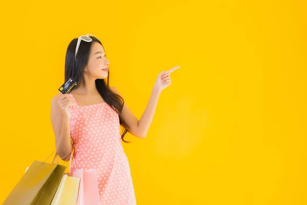 黄色の隔離された背景にスマートフォンやクレジットカードでカラフルなショッピングバッグと肖像画の美しい若いアジアの女性 — ストック写真